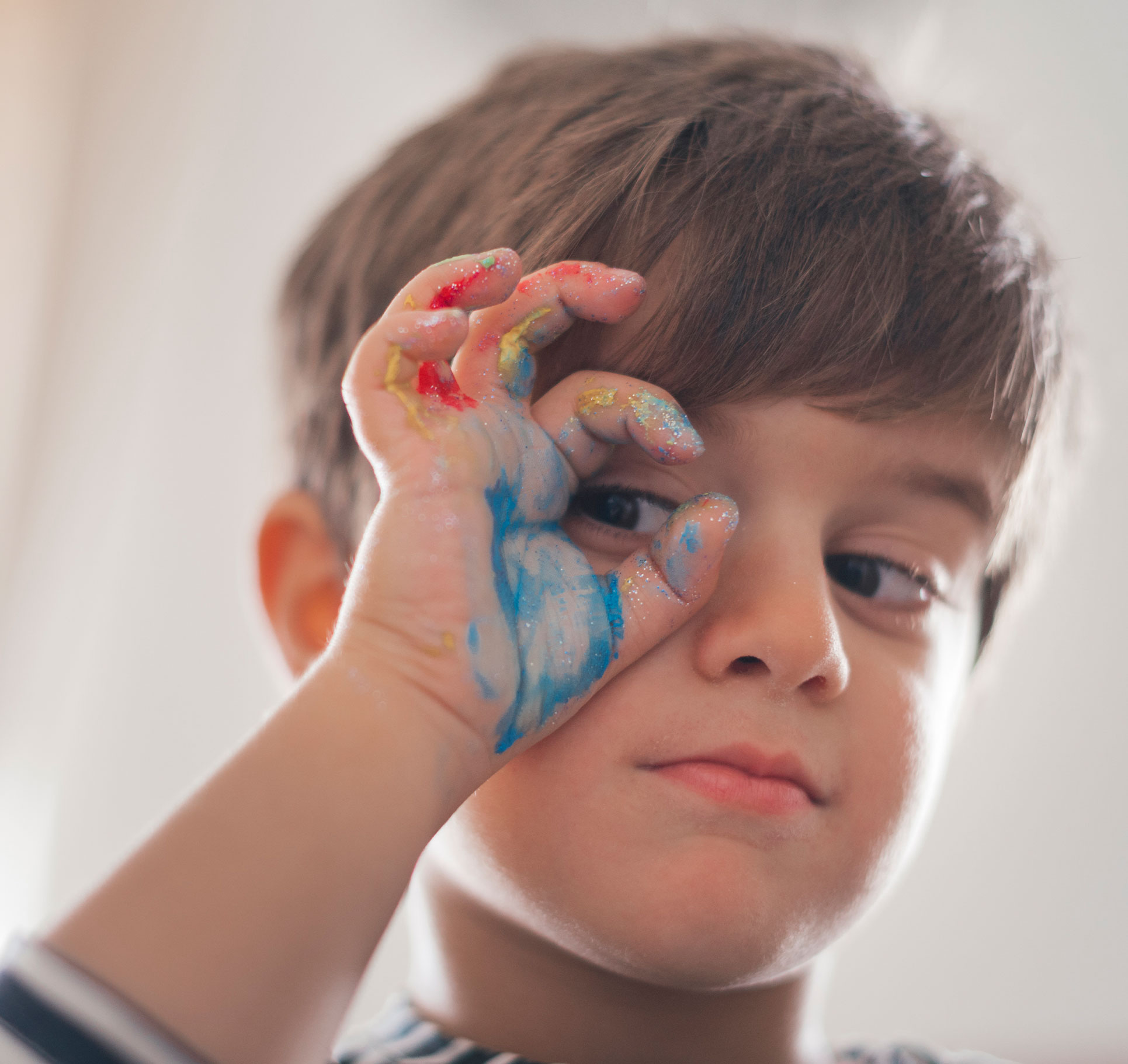 Niño con la mano pintada de colores y puesta en forma de círculo en el ojo